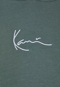 Tissu vert avec un motif cursif blanc brodé centré sur la surface.