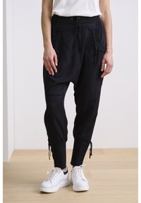 Svarta, avsmalnande byxor med dragsko i midjan, med framfickor och elastiska muddar vid anklarna, stylade med vita sneakers.