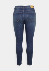 Jeans ajustados de color azul hechos de denim, con una textura suave, dos bolsillos traseros y un parche de cuero marrón claro con la marca en la cintura.