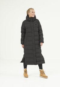 Manteau long noir en doudoune avec un quilting vertical, col montant et fermetures à pression. Doté de poches latérales et d'un design longueur genoux.