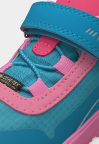 Κοντινό πλάνο ενός μπλε και ροζ αθλητικού παπουτσιού με ελαστικές κορδόνια, ιμάντα με βέλκρο και ορατή ετικέτα Gore-Tex με αόρατη εφαρμογή.