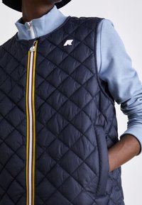 Gesteppte marineblaue Weste mit hohem Kragen, vorderem Reißverschluss und mehrfarbigem Streifendetail in der Mitte. Verfügt über Seitentaschen und ein Logoakzent.