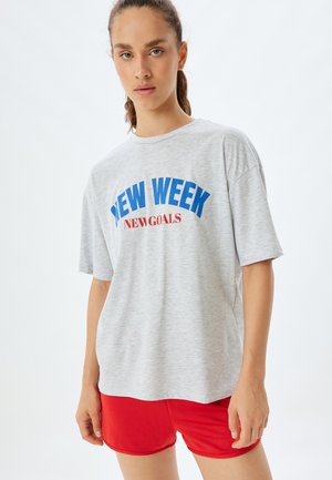 Grå bomulds t-shirt med blå "NEW WEEK" og rød "GOALS" grafisk tryk. Løs pasform, korte ærmer, parret med røde træningsshorts.