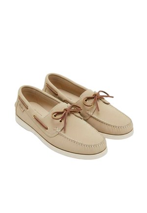 Beige leren bootschoenen met bruine leren veters, witte zolen en mocassinstijl stiksels op een witte achtergrond.