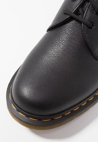 Chaussure en cuir noir avec un bout rond, une surface texturée et des coutures orange contrastantes le long de la semelle. Semelle en caoutchouc pour plus de durabilité.