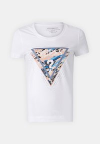 Camiseta blanca de algodón con un gráfico triangular que presenta un patrón abstracto multicolor, el logo "GUESS" y tachuelas decorativas plateadas.