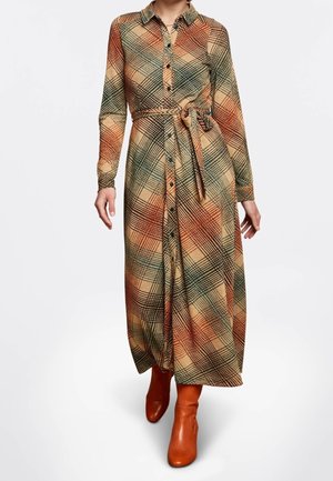 Femme portant une robe-chemise à manches longues à carreaux boutonnée, avec une ceinture nouée à la taille et des bottines marron.