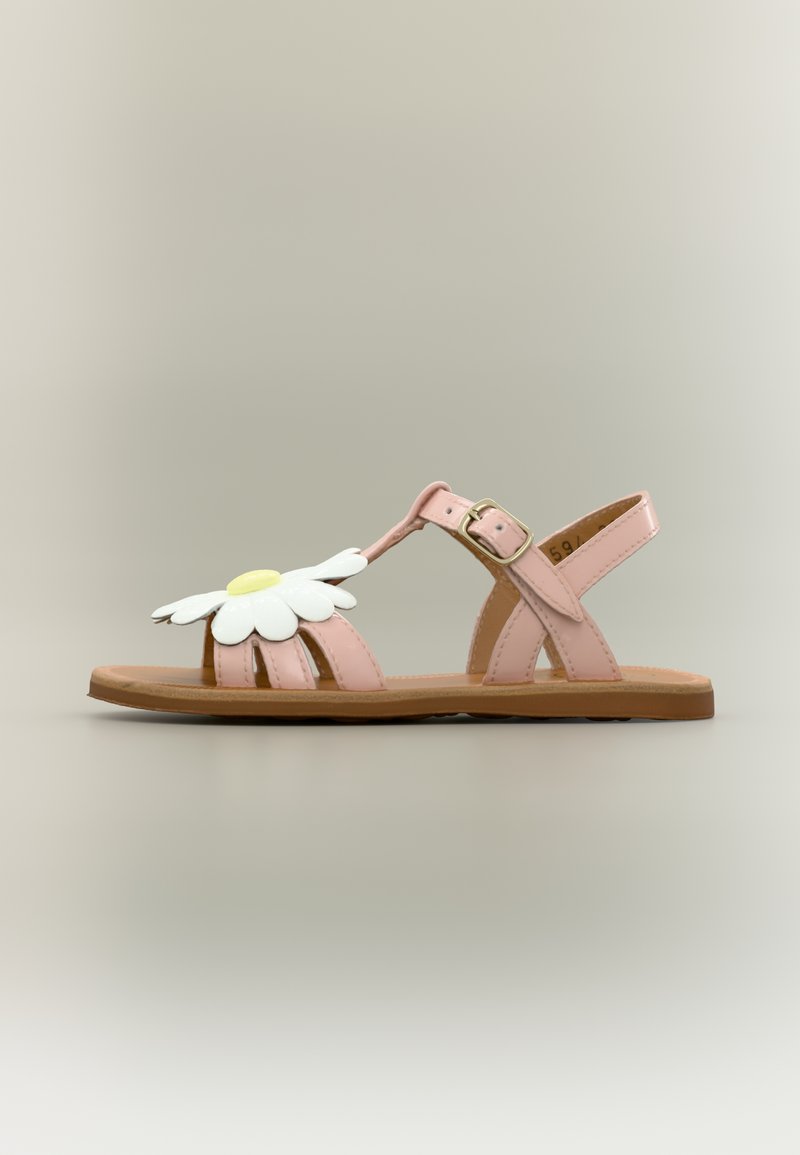 Sandale enfant rose avec bride à boucle et grande décoration marguerite blanche à l'avant, semelle plate marron, vue de côté sur fond uni.