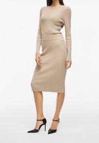 Stickad beige topp och matchande ribbad midikjol; figurnära design med långa ärmar, slät textur och svarta klackar med ankelsnöra.