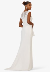 Long white dress featuring a fitted silhouette, lace bodice with floral detailing, sheer back panel, and a flowing skirt.