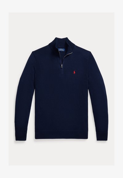 Tamsiai mėlynas mezginys megztinis su aukštu apykaklių ir ketvirtiniu užtrauktuku. Ant kairiojo krūtinės krašto yra mažas raudonas logotipas, o rankovės galai ir apačia yra riboti.