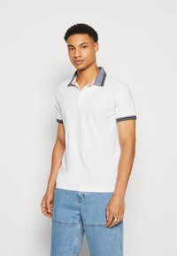 Tricou polo alb cu guler și mansete bleumarin, având un design texturat. Trei nasturi la gât și un logo pe piept.