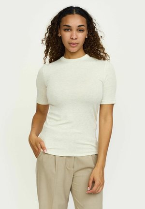 Világos bézs színű, rövid ujjú póló, puha anyagból, kerek nyakú és slim fit fazonú, bézs, magas derekú nadrággal párosítva.