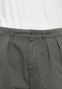 Pantaloni grigi plissettati con una texture liscia, chiusura a un bottone e tasche laterali per un design pratico.