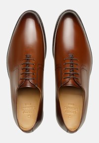 Chaussures habillées en cuir marron avec une finition lisse, bout arrondi, cinq œillets et de subtils détails de couture autour de la zone des lacets.