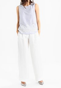 Top senza maniche a righe blu chiaro con bordo in pizzo bianco, abbinato a pantaloni bianchi larghi e tacchi argento. Tessuto morbido e vestibilità rilassata.