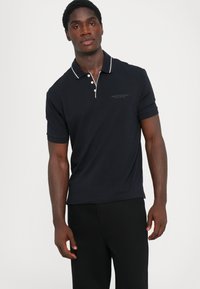Marineblå polo-shirt med en kontrasterende hvit krage, korte ermer og en subtil logo. Glatt bomullsmateriale, tettsittende design.