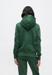 Sweatshirt verde feito de tecido macio, com capuz grande, punhos e bainha canelados. Usado com calças verdes combinando.