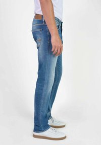 Jeans de mezclilla azul claro con un ligero acabado desgastado, diseño de pierna recta, bolsillos traseros visibles y un parche de cuero marrón en la cintura.