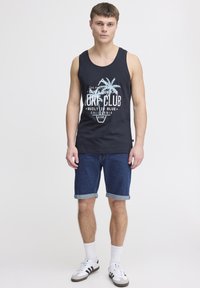 Námořnická tílko s motivem palmy a textem "Surf Club", doplněné o roztrhané džíny. Model má na sobě bílé ponožky a tenisky.