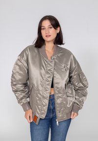 Satynowa kurtka bomberka w jasnoszarym kolorze z prążkowanymi mankietami i kołnierzem. Posiada pomarańczową metkę z boku i kieszeń na suwak na rękawie.
