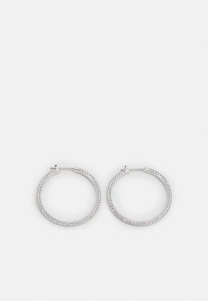 Hopeiset korvarenkaat, joihin on kiinnitetty pieniä kirkkaanvärisiä kristalleja, asetettu vierekkäin valkoisella taustalla.