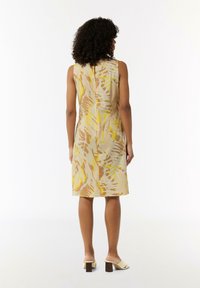Ärmelloses Kleid in hellem Beige mit abstrakten gelben und braunen Blättern. Glattes Material; knielang, gerade geschnitten; Rückenschlitz-Detail.