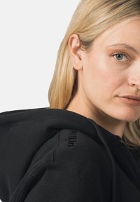 Felpa con cappuccio nera con cerniera e tessuto morbido. Dotata di cappuccio, logo ricamato sulla spalla e dettagli di cuciture visibili.