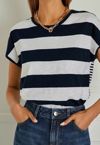 Camiseta a rayas en azul marino y blanco con un corte relajado, tejido suave, mangas cortas y escote redondo, combinada con jeans de cintura alta.