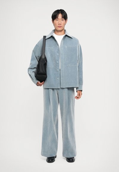 Light blue corduroy oversized jacket with two front pockets, paired with matching wide-leg pants and a small black shoulder bag.