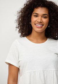 Hellbeige, kurzärmliges Kleid mit tailliertem Oberteil und einem weit schwingenden, gerafften Rock. Weicher Stoff mit glatter Textur. Rundhalsausschnitt.