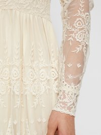 Vestido de encaje marfil con intrincados bordados florales, mangas largas transparentes y una falda plisada con detalles texturizados en los puños.