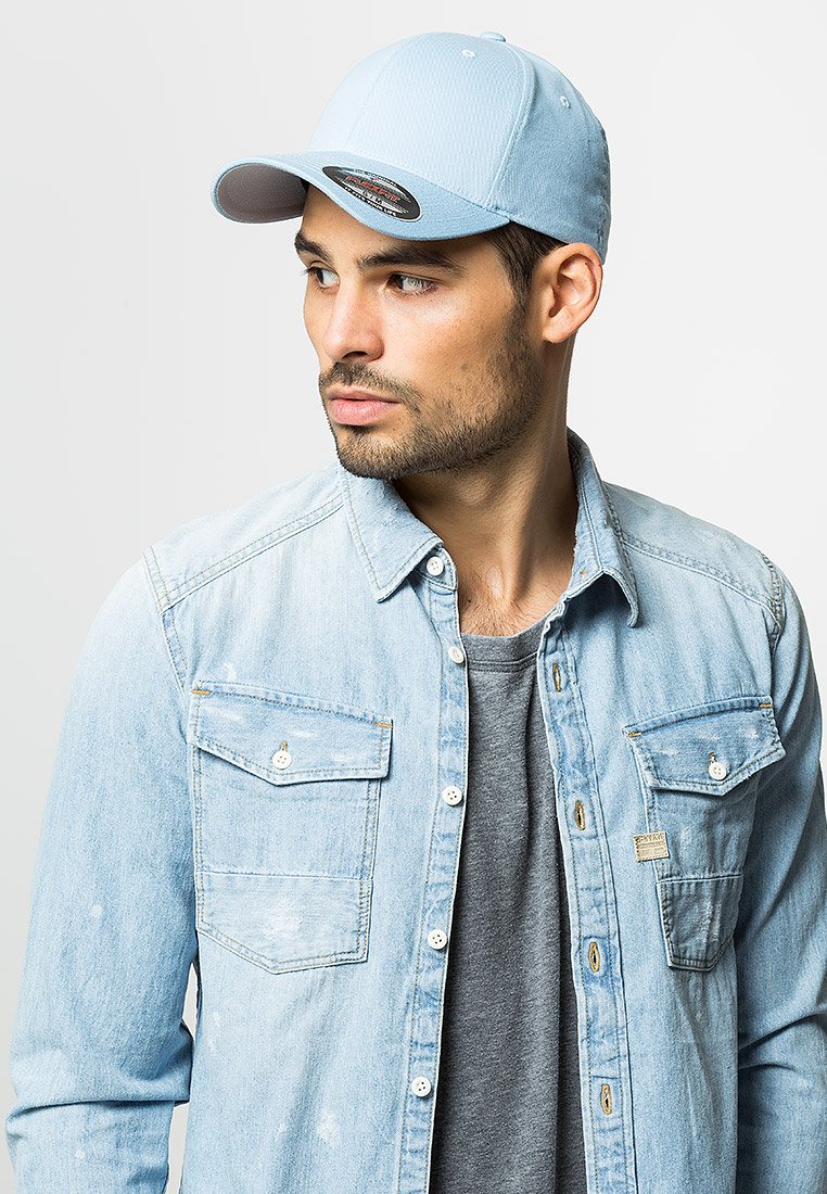 Light blue baseball cap with a curved visor, featuring subtle textured fabric. Worn with a denim shirt and gray t-shirt underneath.