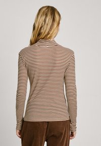 Top de manga larga a rayas marrón y crema con collar alto, diseño ajustado y textura acanalada, combinado con pantalones de pana marrones.