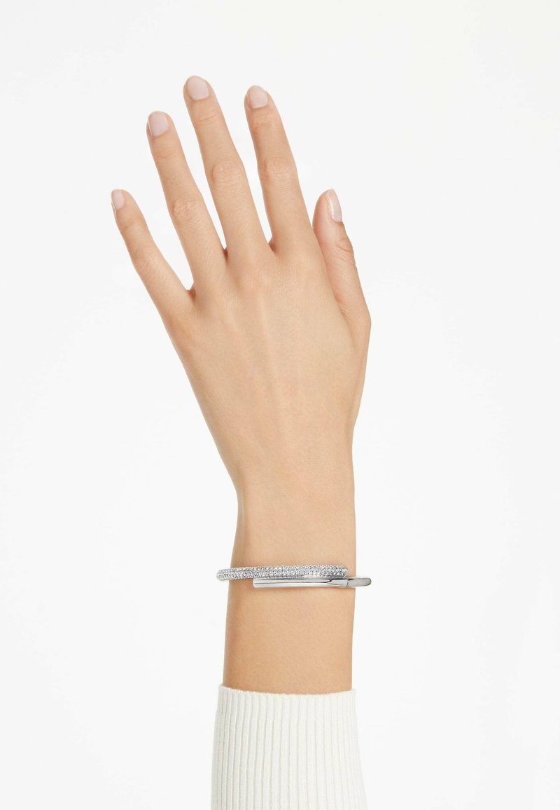Pulsera de plata con una banda metálica suave y una sección texturizada y brillante. Llevada en una mano con esmalte de uñas en tono neutro.