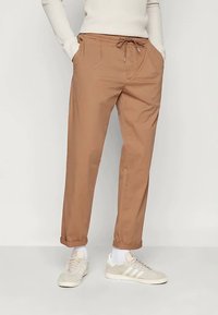 Svetlo rjave lahke hlače z vrvico v pasu, stranskimi žepi in manšetami na koncih, v kombinaciji s svetlimi supergami in belimi nogavicami.