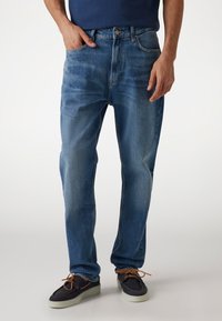 Light blue denim jeans with a straight-leg cut, five pockets, and subtle fading. Paired with dark shoes featuring brown laces.