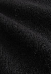 Čierna vlnená látka s jemnou a chlpatou textúrou, s jemným leskom a nepravidelným rebrovaným vzorom, zdôrazňujúca jej teplo a hrúbku.