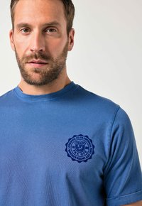 Blue cotton t-shirt featuring round neckline and dark blue printed logo on the chest. Smooth texture with short sleeves.