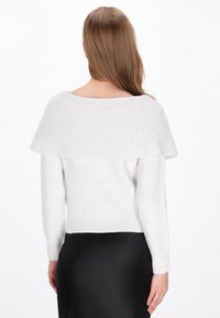 Pull en tricot blanc avec un col large à épaules dénudées, des manches longues et des détails texturés sur l'ensemble. Silhouette ajustée à la taille.
