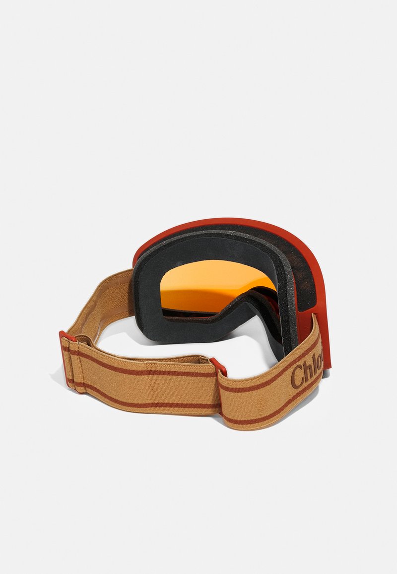 Skibrille mit orangefarbener Linse, schwarzem und rotem Rahmen sowie einem beigen elastischen Band mit braunen Streifen und "Chloé"-Branding.