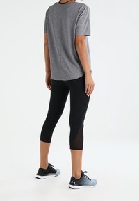 Szary krótki top z krótkim rękawem, czarne legginsy i niebieskie buty sportowe. Legginsy mają teksturowe panele; top ma prosty krój i zaokrąglony dół.