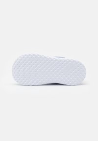 Suela de zapatilla blanca con un patrón en zigzag texturizado, que presenta una puntera redondeada y un diseño plano para mayor tracción. Branding mínimo visible.
