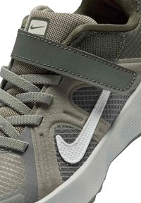 Γκρι και πράσινο αθλητικό παπούτσι Nike με υφασμάτινο δίχτυ, κορδόνια, ιμάντα με βέλκρο και λευκό, ανάγλυφο λογότυπο Nike Swoosh στο πλάι.