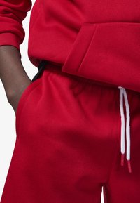 Sudadera roja con bolsillo frontal y pantalones de chándal rojos a juego, que cuentan con una cinturilla elástica y cordones blancos con puntas rojas.