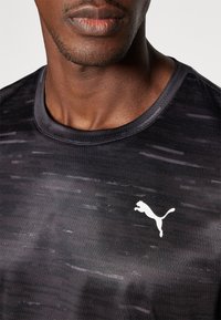 Zwart sportshirt met een gestructureerd ontwerp. Heeft een ronde hals, korte mouwen en een wit Puma-logo op de borst.