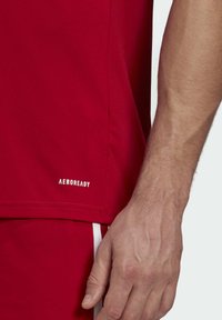 Maglietta sportiva rossa AEROREADY con una texture liscia e un logo stampato in bianco sull'orlo. Design aderente con un leggero lucido.