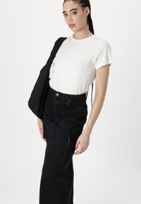 Hvit kortermet t-skjorte kombinert med svarte høy midje jeans med lomme, som holder en svart quilted skulderveske.