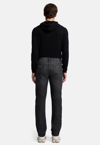 Schwarzer Hoodie mit Kapuze, kombiniert mit dunkelgrauen Jeans mit zwei Gesäßtaschen. Das Outfit wird mit hellen Sneakers abgerundet.