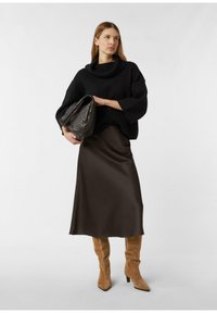 Czarny, dziany, oversize'owy sweter z golfem, brązowa, satynowa spódnica midi, brązowe zamszowe kozaki za kolano, trzyma teksturowaną, ciemną torbę.